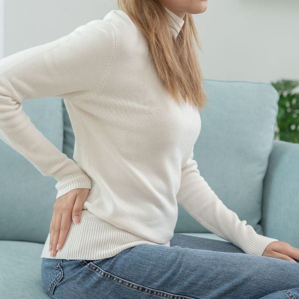 sitting on couch with hand on lower back, in pain